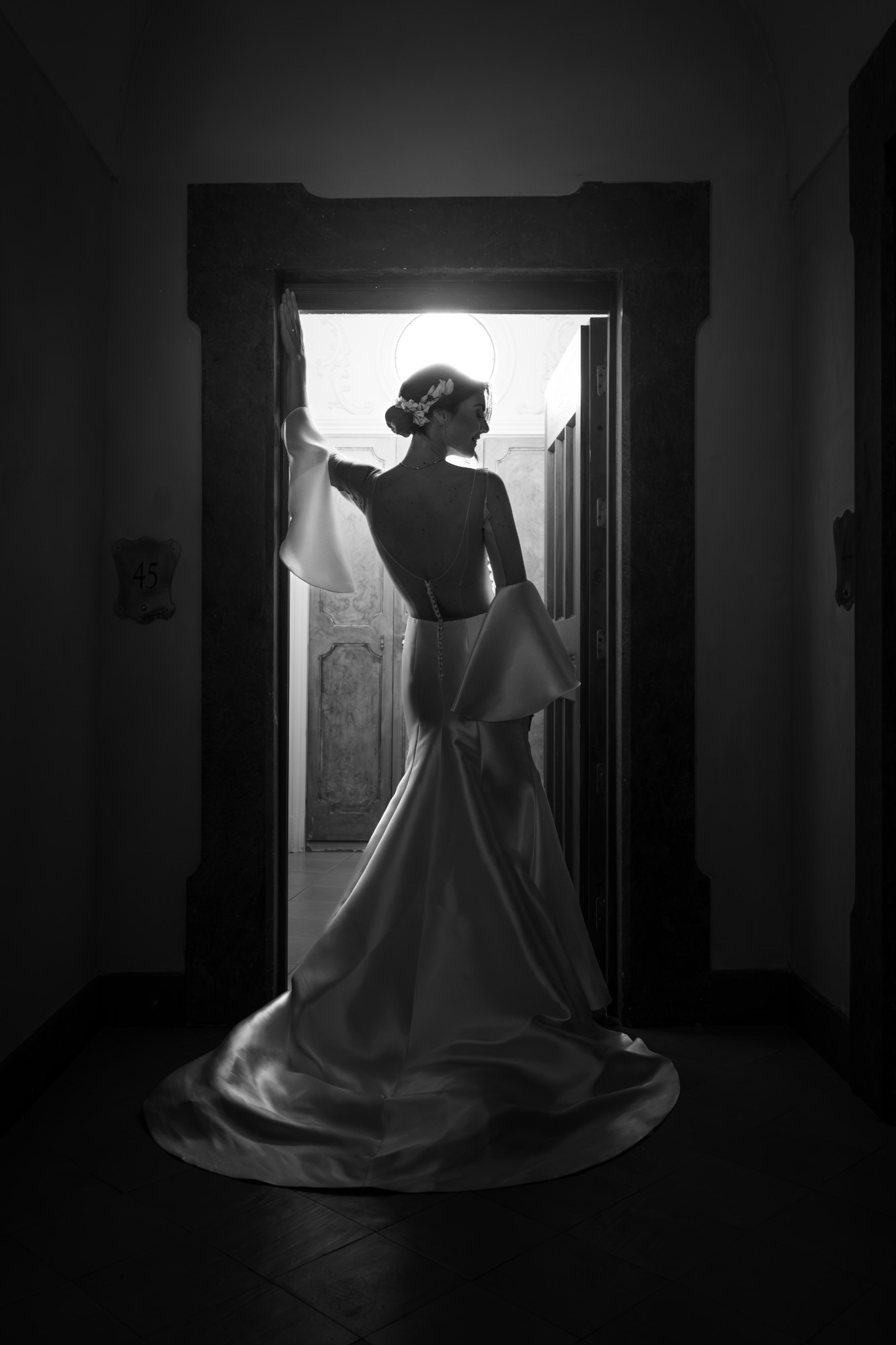 La sposa di spalle in controluce sulla soglia di una porta, in bianco e nero